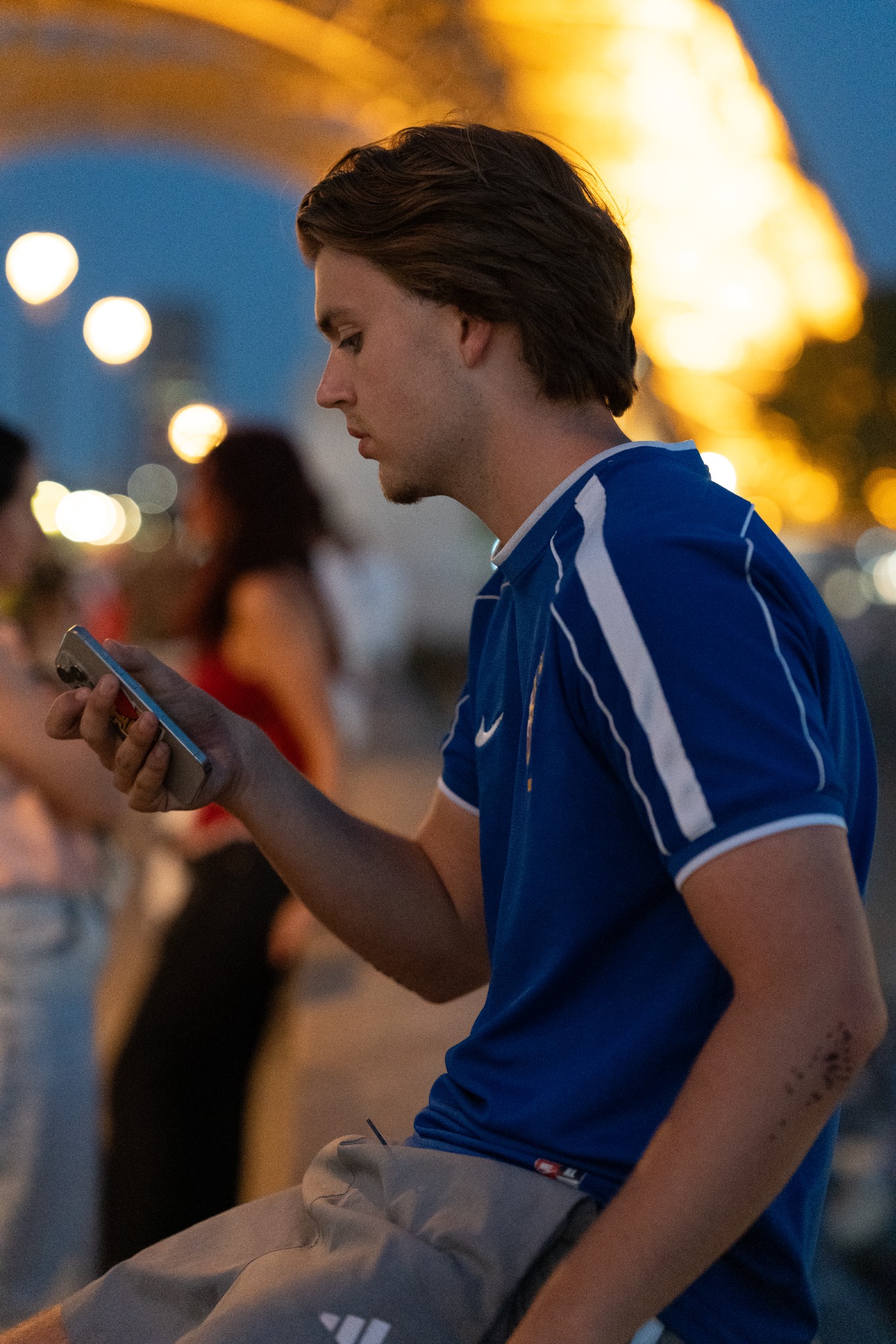Young man in a blue shirt at the Eiffel Tower after dark