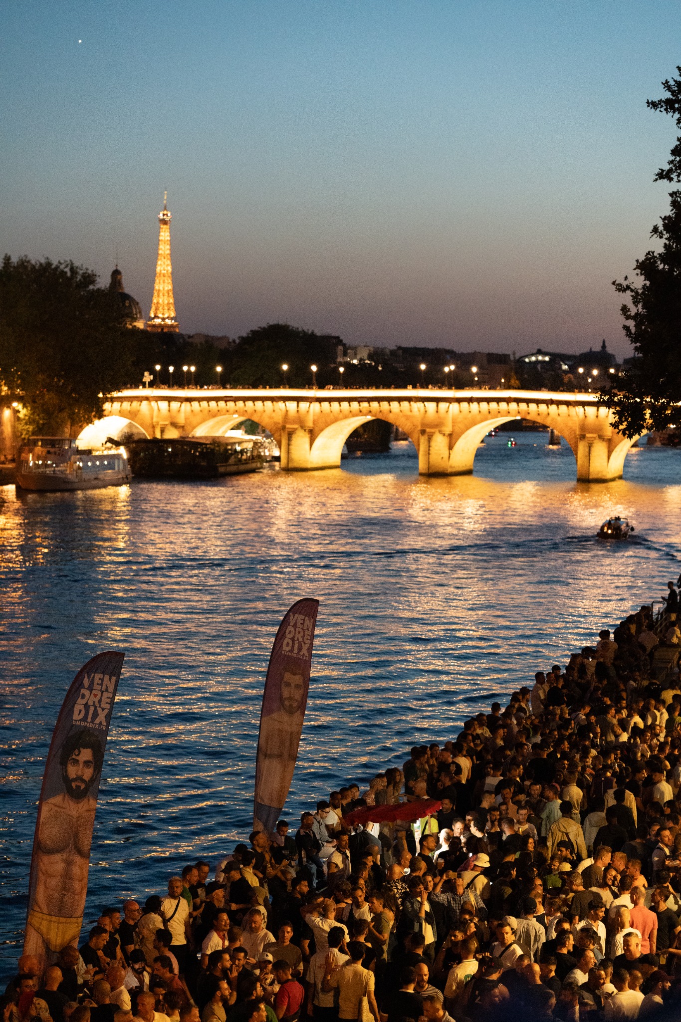 Crowd by the Seine as Paris lights reflect on the water
